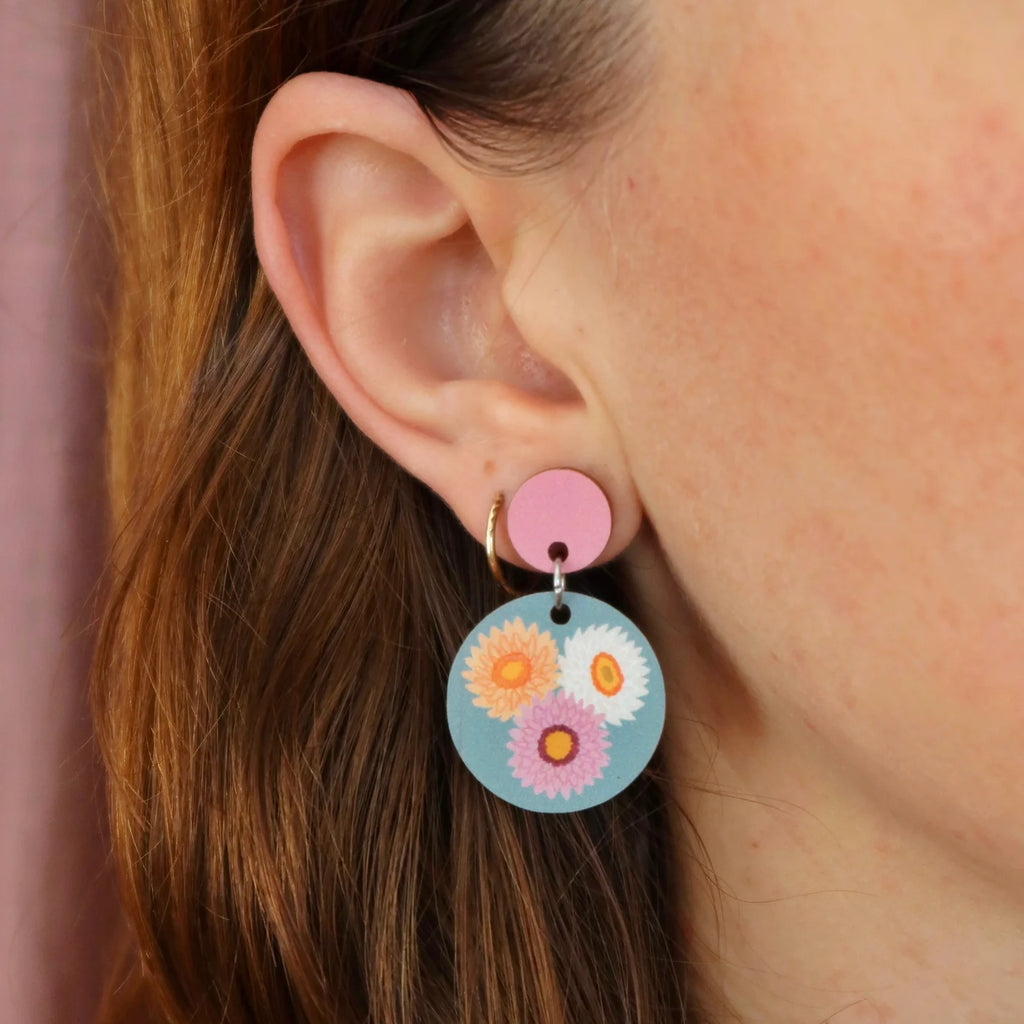 Close-up of an ear wearing a colorful floral earring with a pink background