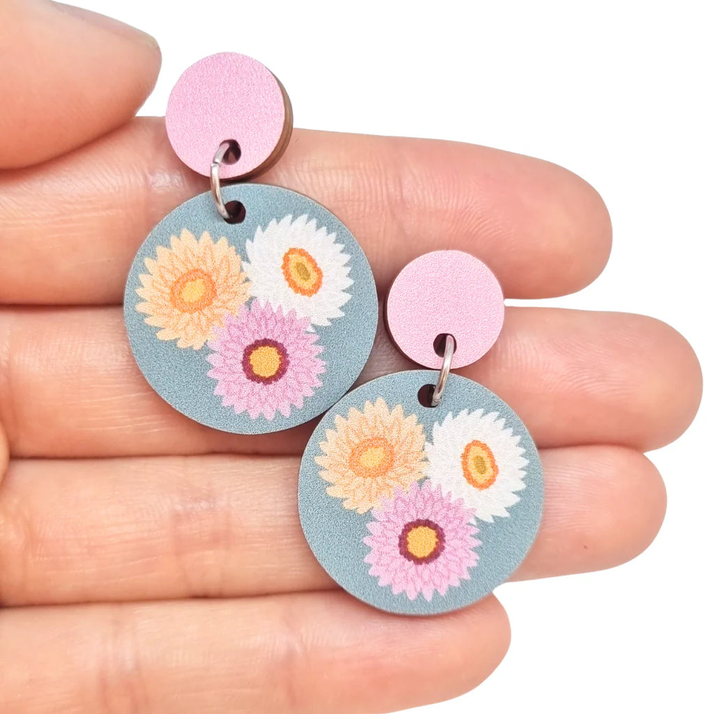 Floral earrings held between fingers against a white background