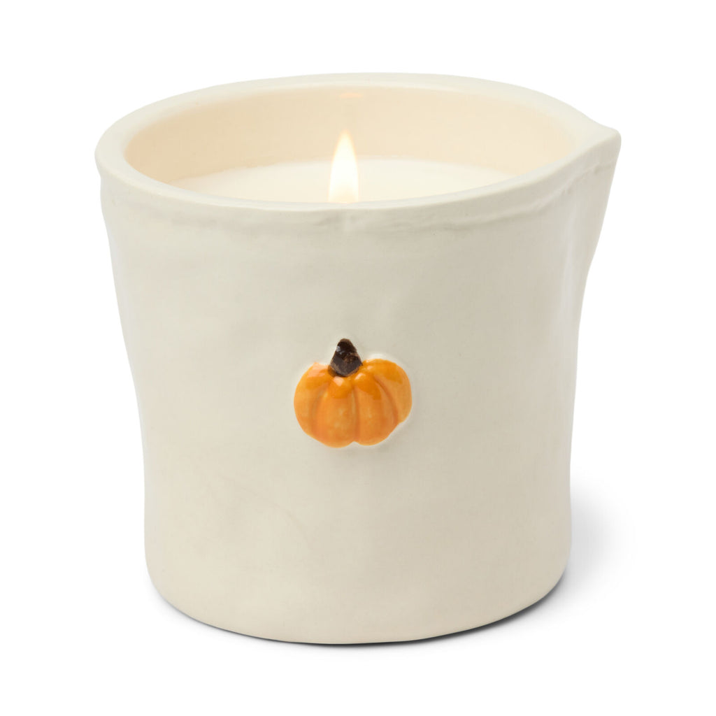 Candle in a white container with a small orange pumpkin on a white background