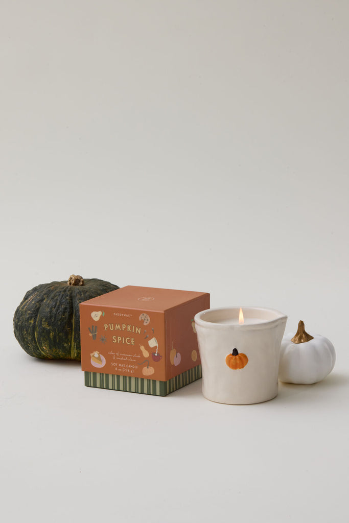 Candle with pumpkin spice packaging and decorative pumpkins on a light background