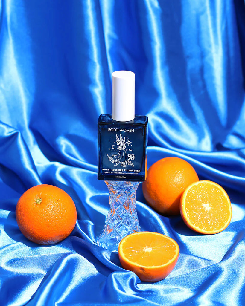 Bottle of Borbo perfume with oranges on a blue satin background