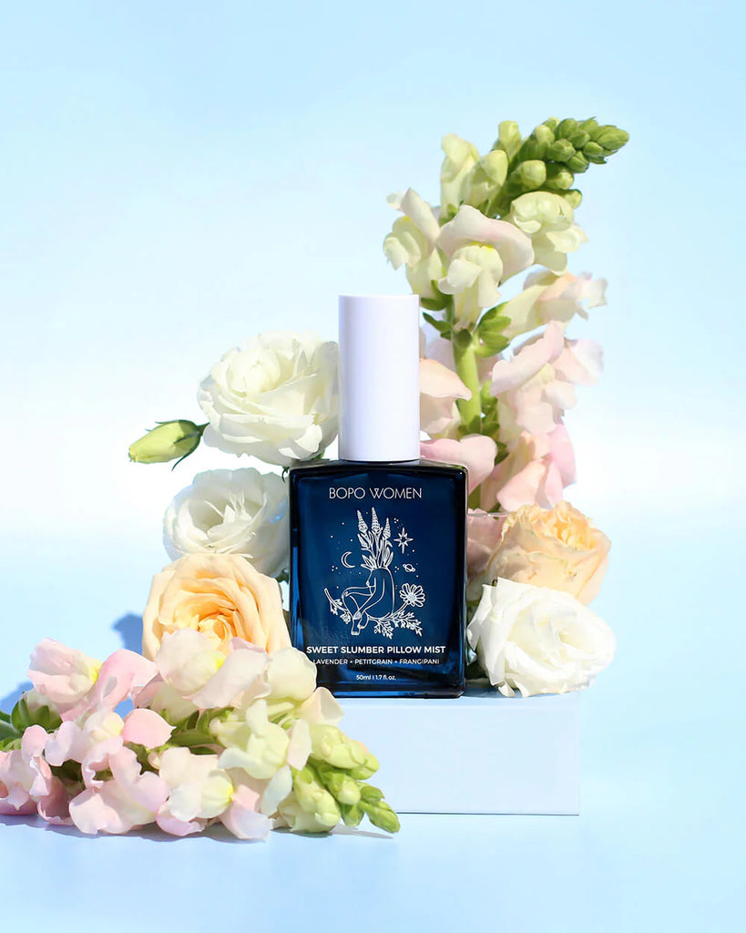 Bottle of Borbo Women Sweet Summer Pillow Mist surrounded by flowers on a light blue background