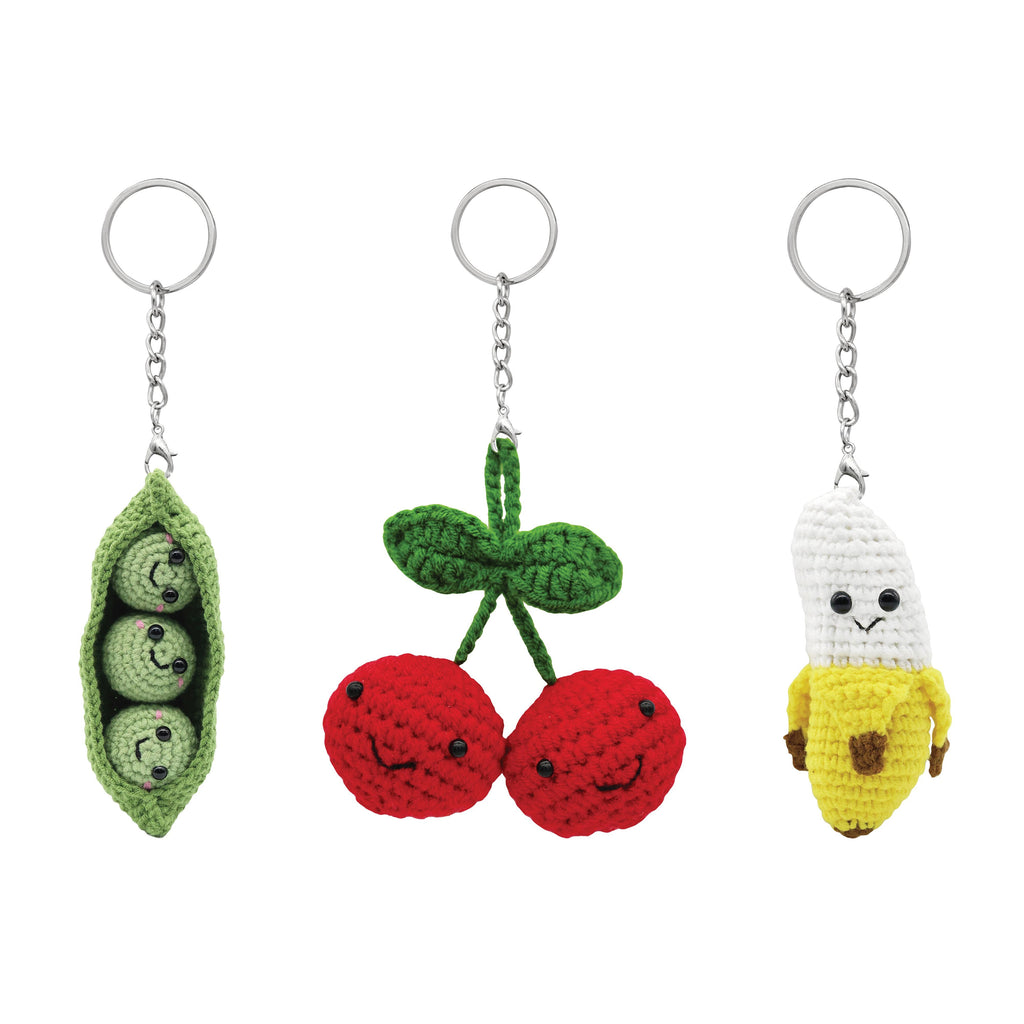 Three crochet keychains shaped like peas, cherries, and a banana on a white background.